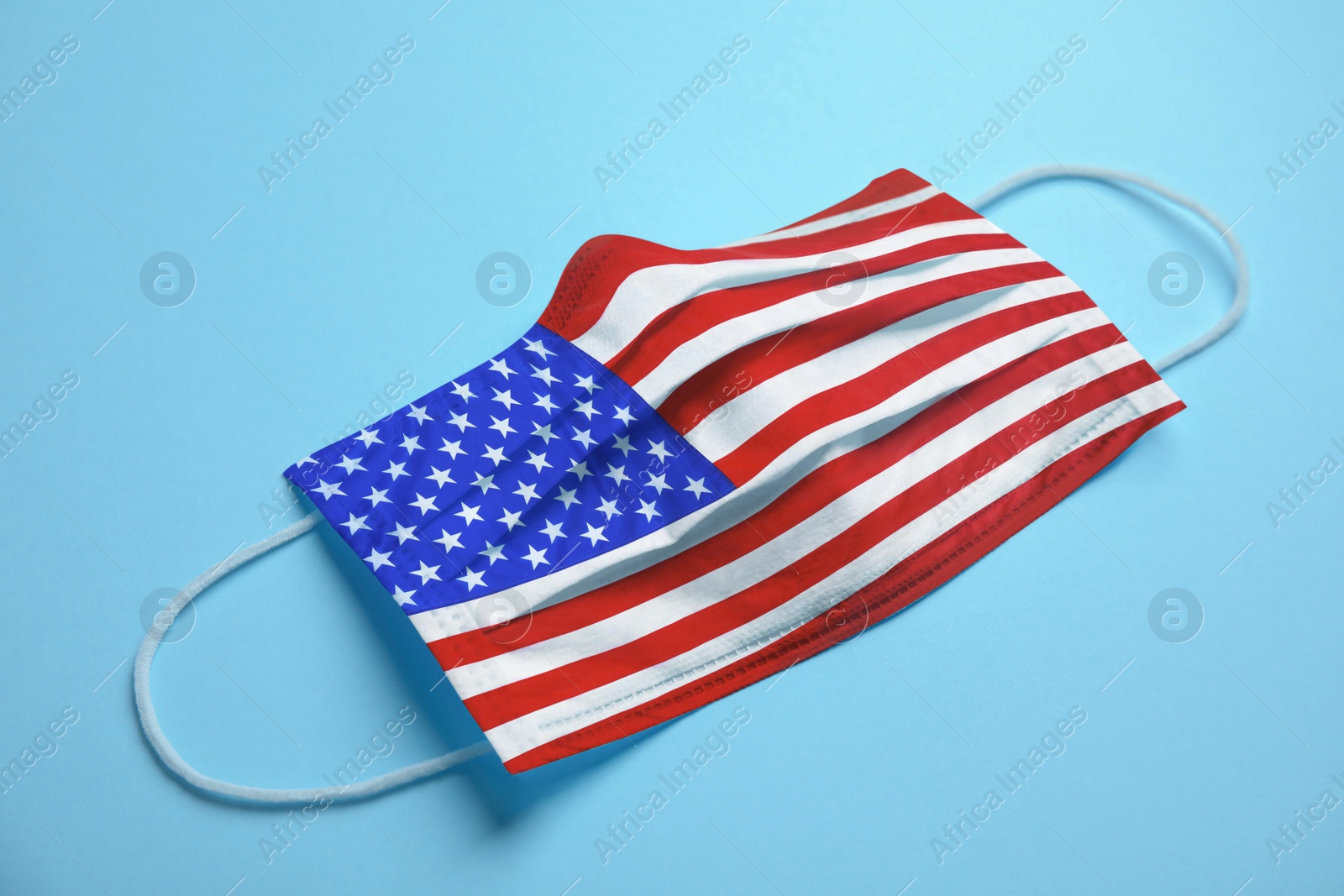 Image of Medical protective mask with USA flag pattern on light blue background. Dangerous virus