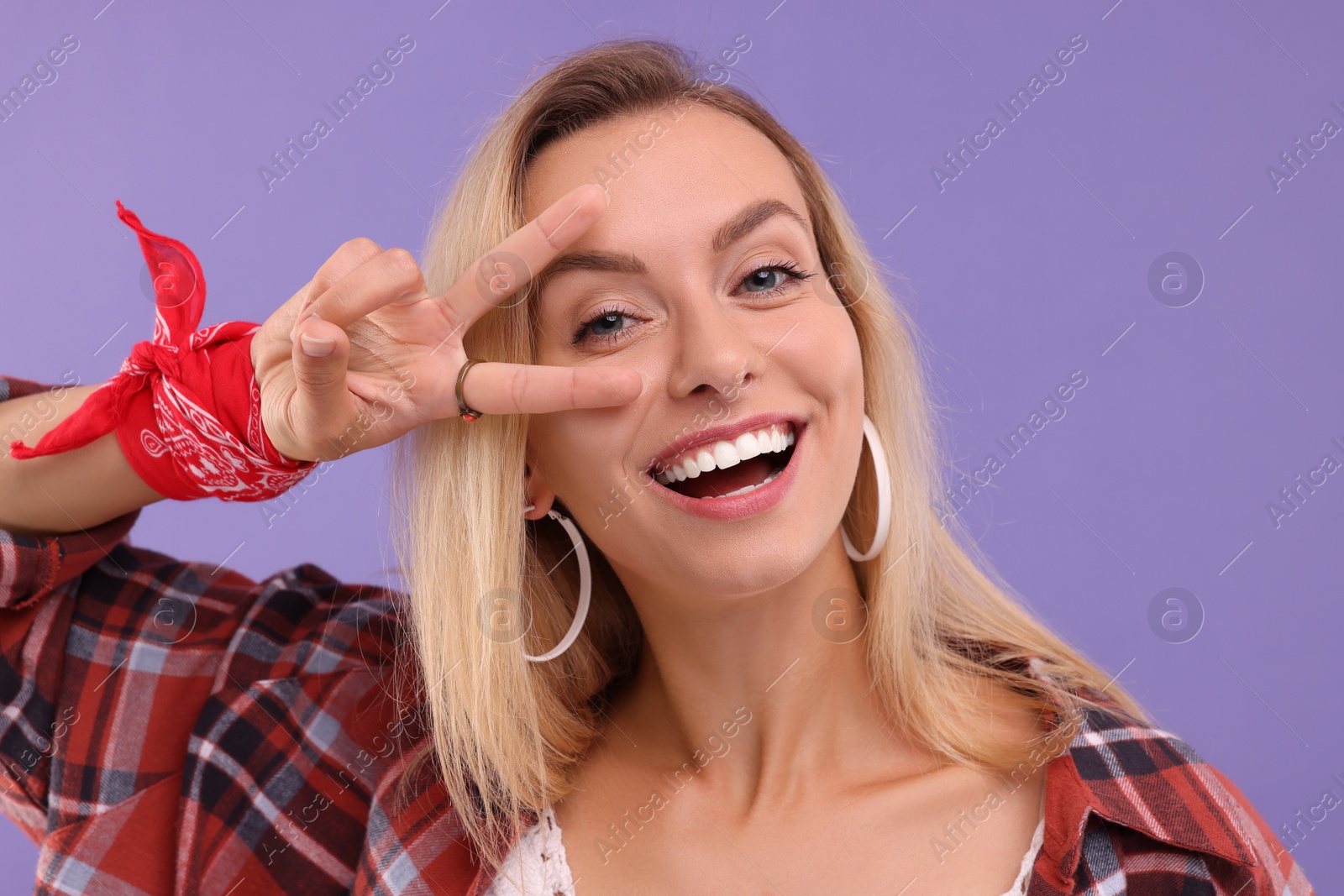 Photo of Portrait of happy hippie woman showing peace sign on purple background