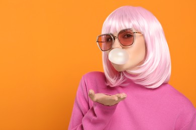 Beautiful woman in sunglasses blowing bubble gum on orange background, space for text