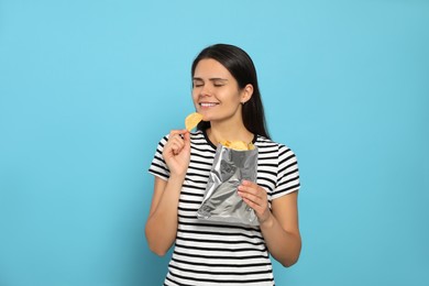 Beautiful woman eating potato chips on light blue background