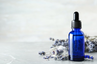 Bottle of natural essential oil and lavender flowers on grey marble background. Space for text