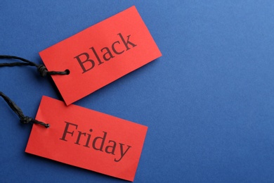 Photo of Red tags with words BLACK FRIDAY on blue background, flat lay. Space for text