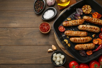 Photo of Tasty grilled sausages and ingredients on wooden table, flat lay. Space for text