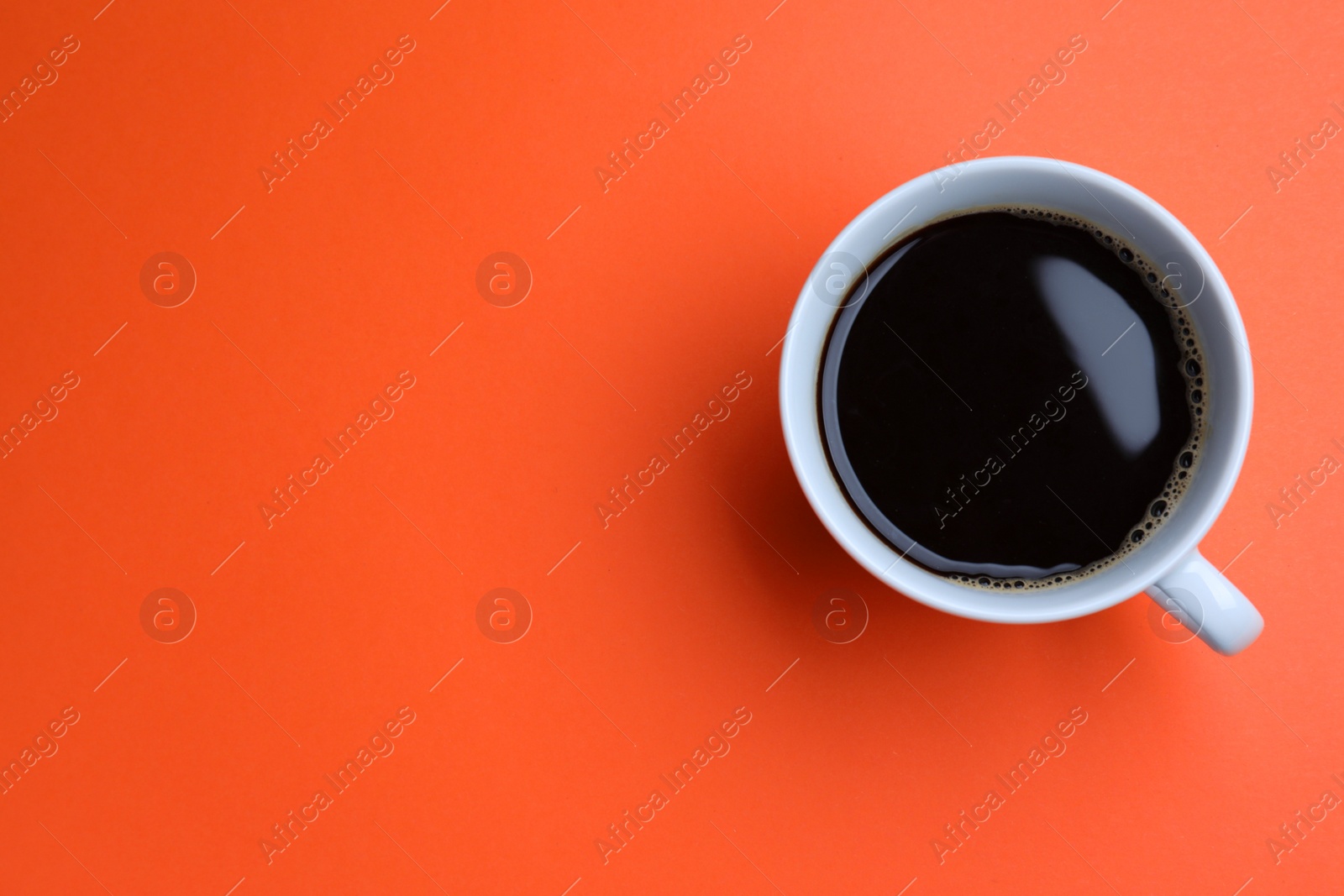 Photo of White mug of freshly brewed hot coffee on orange background, top view. Space for text