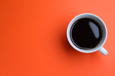 Photo of White mug of freshly brewed hot coffee on orange background, top view. Space for text