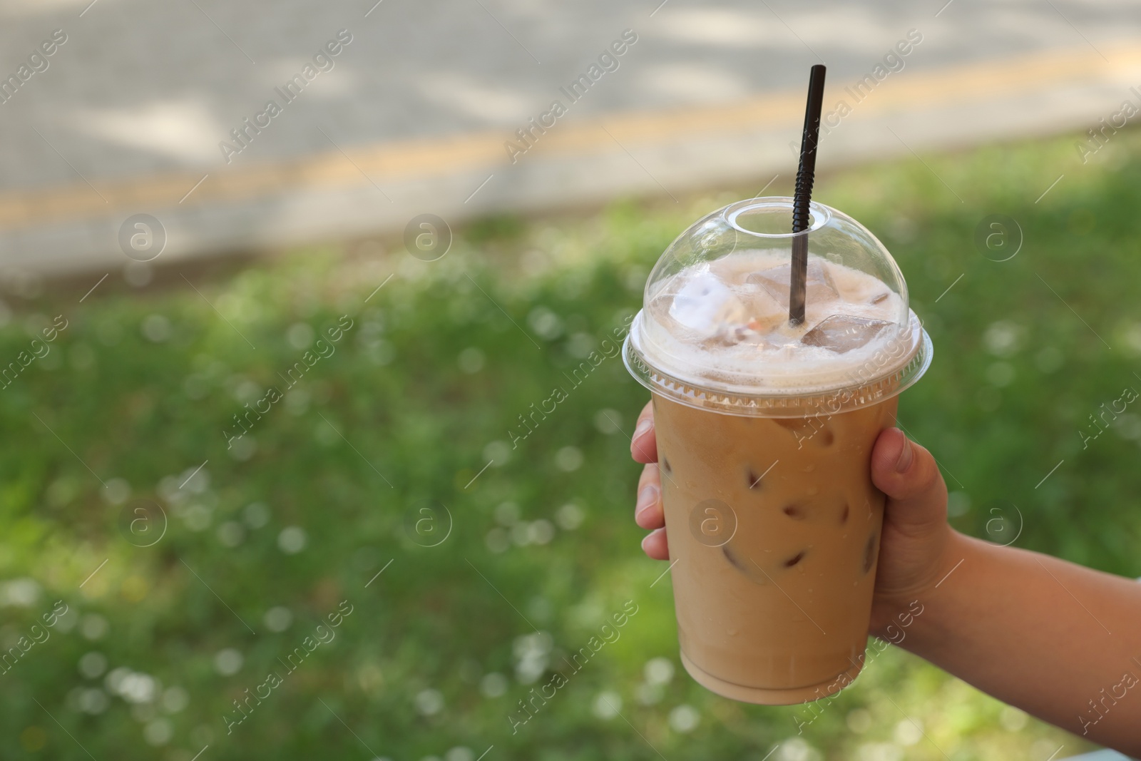 Photo of Woman holding plastic takeaway cup of delicious iced coffee outdoors, closeup. Space for text