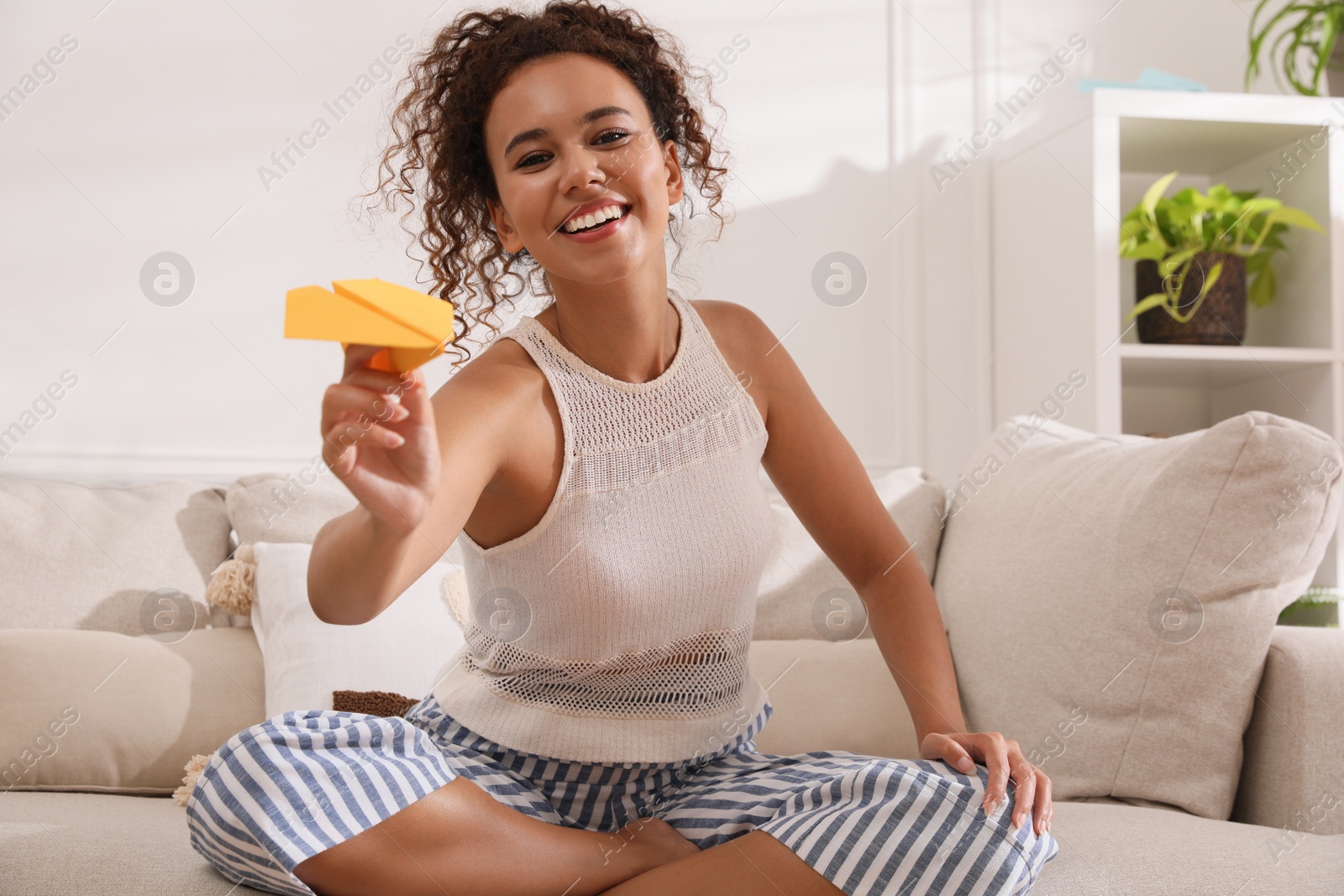 Photo of Beautiful African-American woman playing with paper plane in living room at home