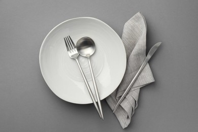 Clean bowl and cutlery on grey background, top view
