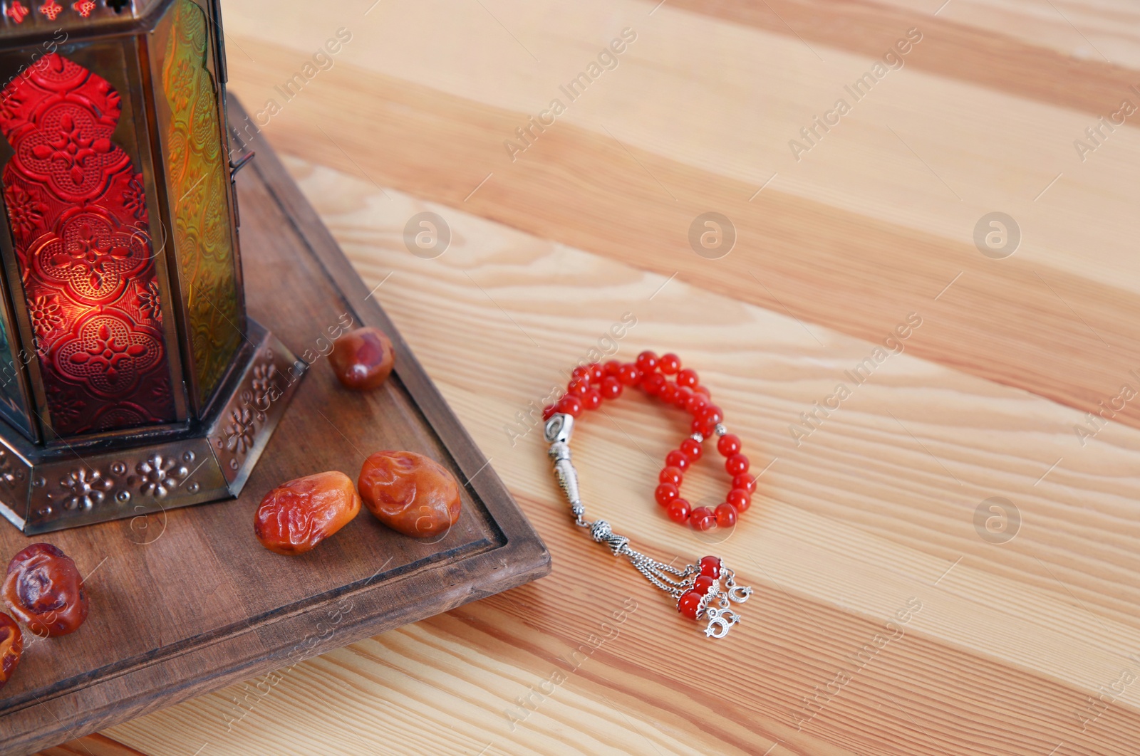 Photo of Muslim lantern Fanous, dried dates and prayer beads on wooden table. Space for text