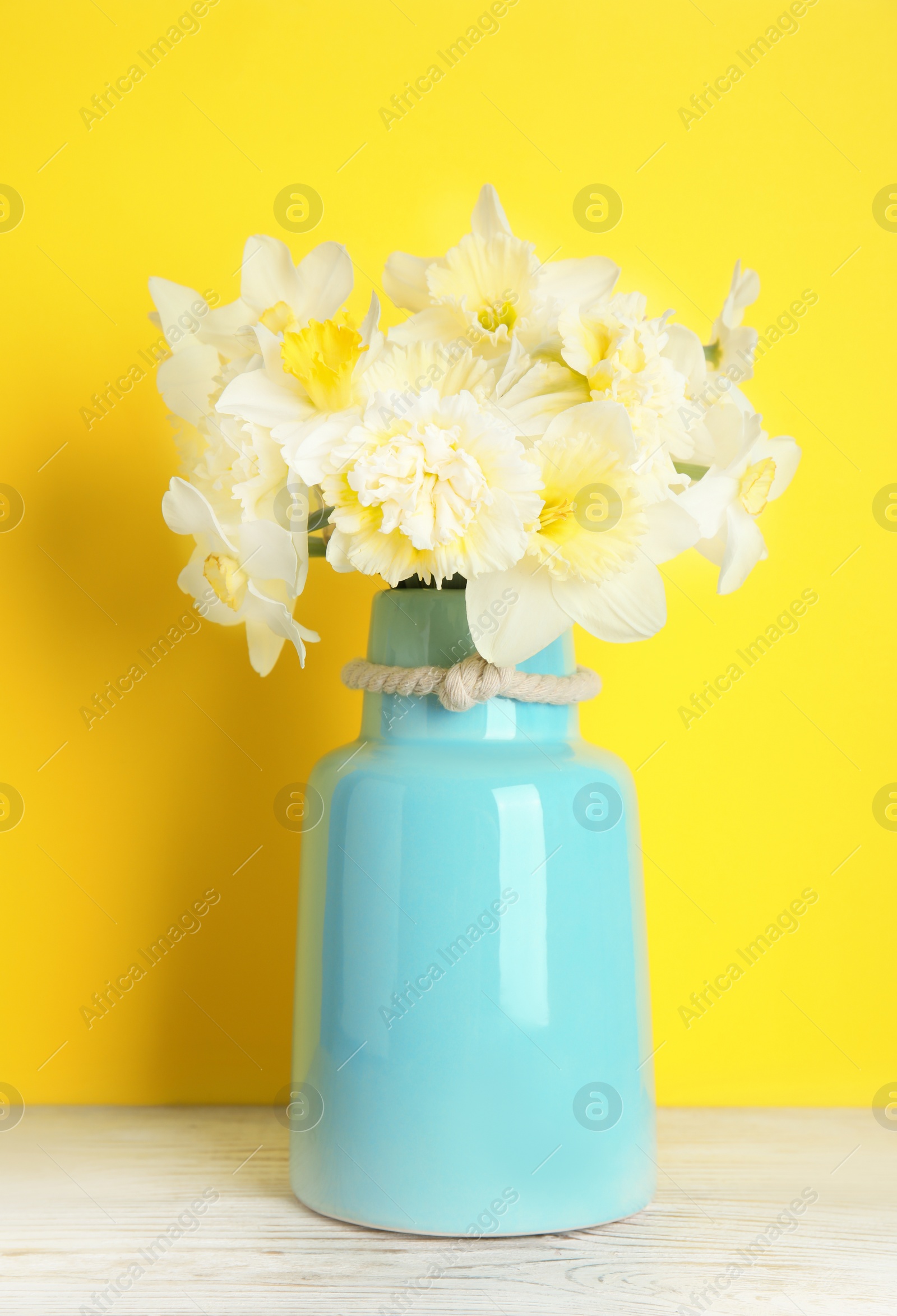 Photo of Bouquet of daffodils in vase on table against color background. Fresh spring flowers