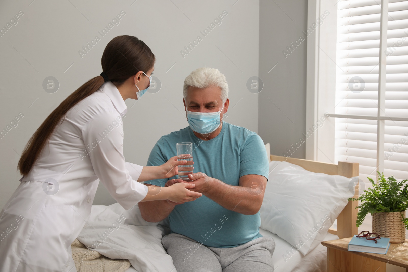 Photo of Doctor giving water to senior man with protective mask at nursing home