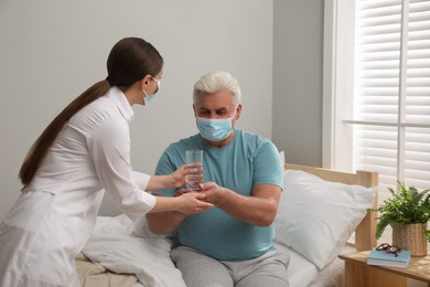 Doctor giving water to senior man with protective mask at nursing home