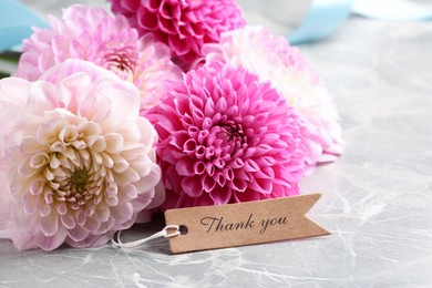 Paper tag with phrase Thank You and bouquet of dahlias on marble table, closeup