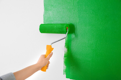 Photo of Woman painting white wall with green dye, closeup. Interior renovation