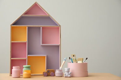 Composition with house shaped shelf and jars of paints on table, space for text. Interior element