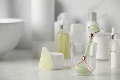 Photo of Natural face roller, gua sha tool and cosmetic products on counter in bathroom. Space for text