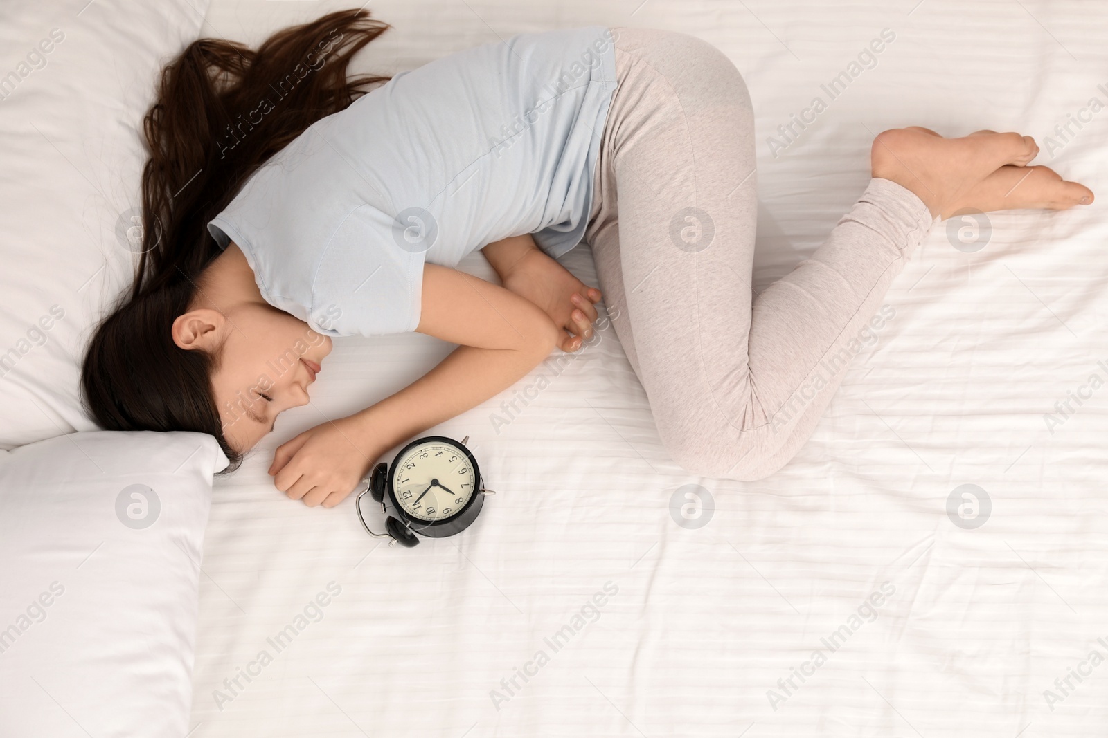 Photo of Beautiful little girl with alarm clock sleeping in bed, top view