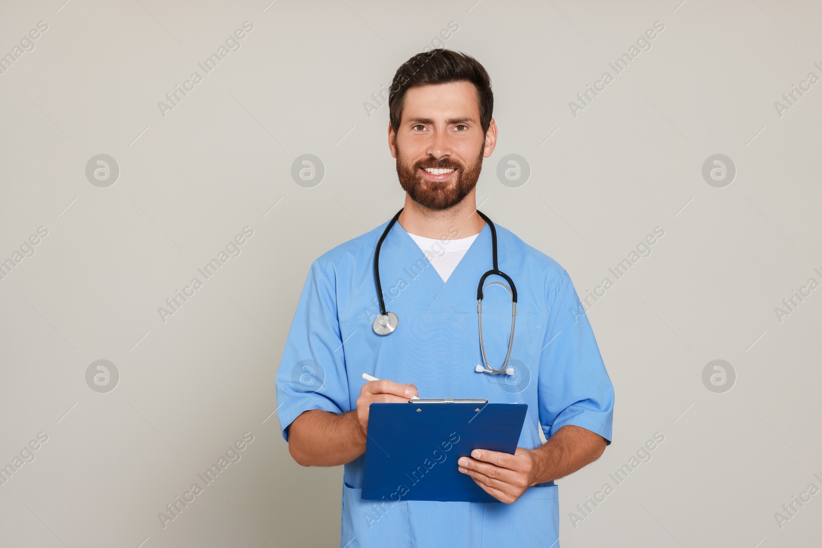 Photo of Happy doctor with stethoscope and clipboard on light grey background