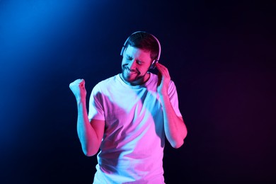 Photo of Happy man in headphones enjoying music in neon lights against dark blue background