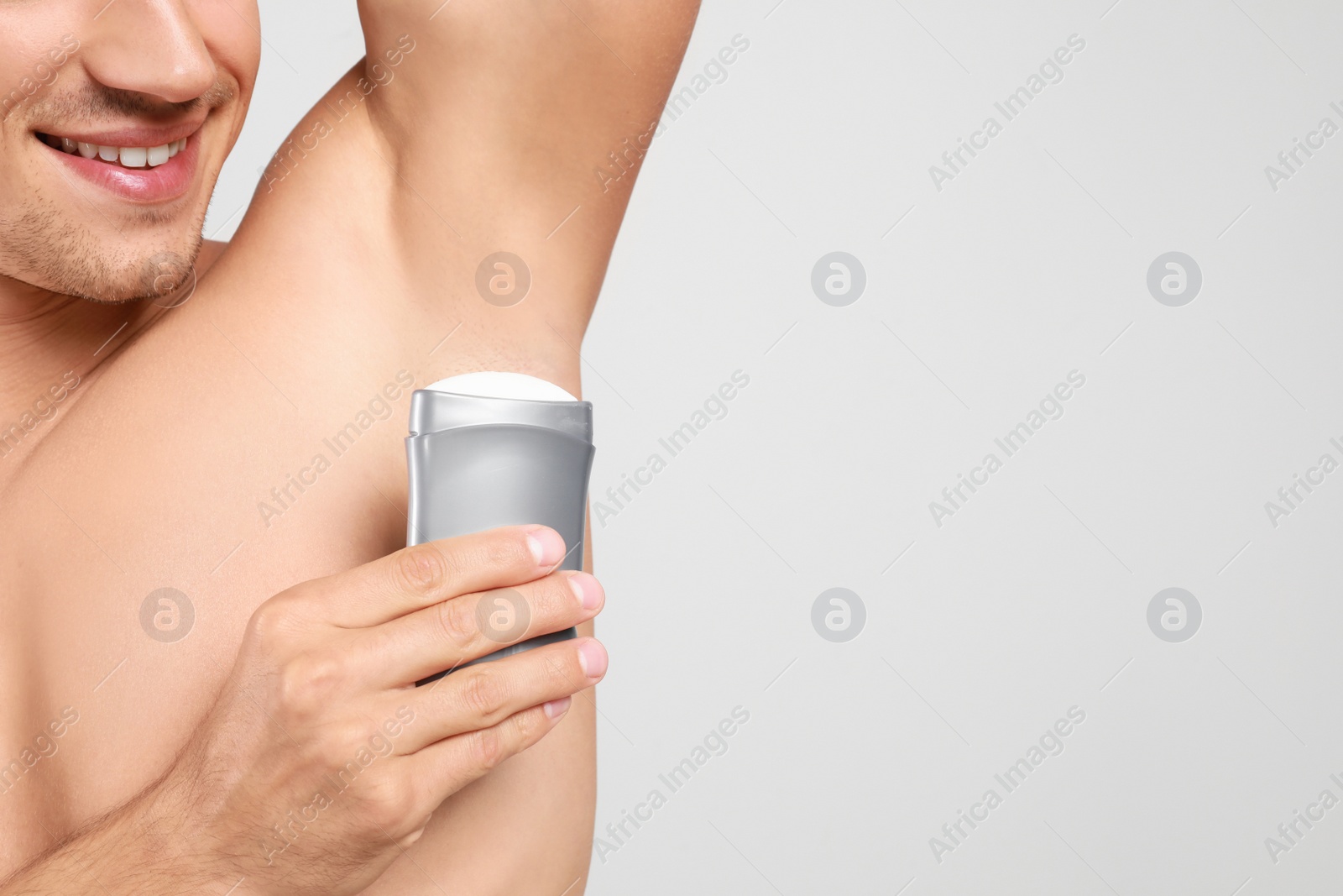 Photo of Young man applying deodorant to armpit on light background, closeup. Space for text