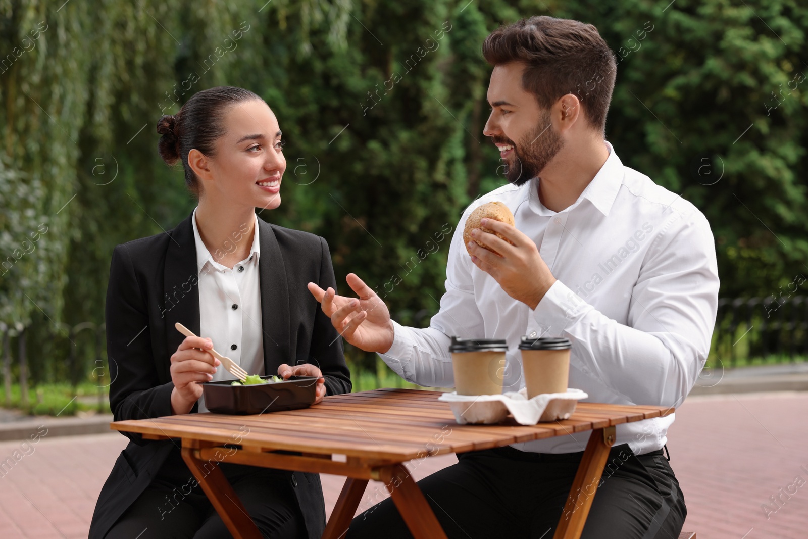 Photo of Business lunch. Happy colleagues spending time together at wooden table during break outdoors