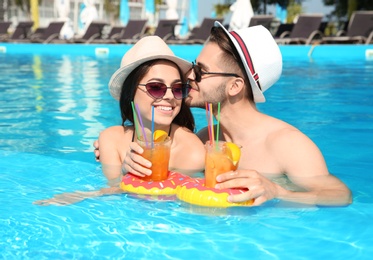 Photo of Young couple with refreshing cocktails in swimming pool on sunny day