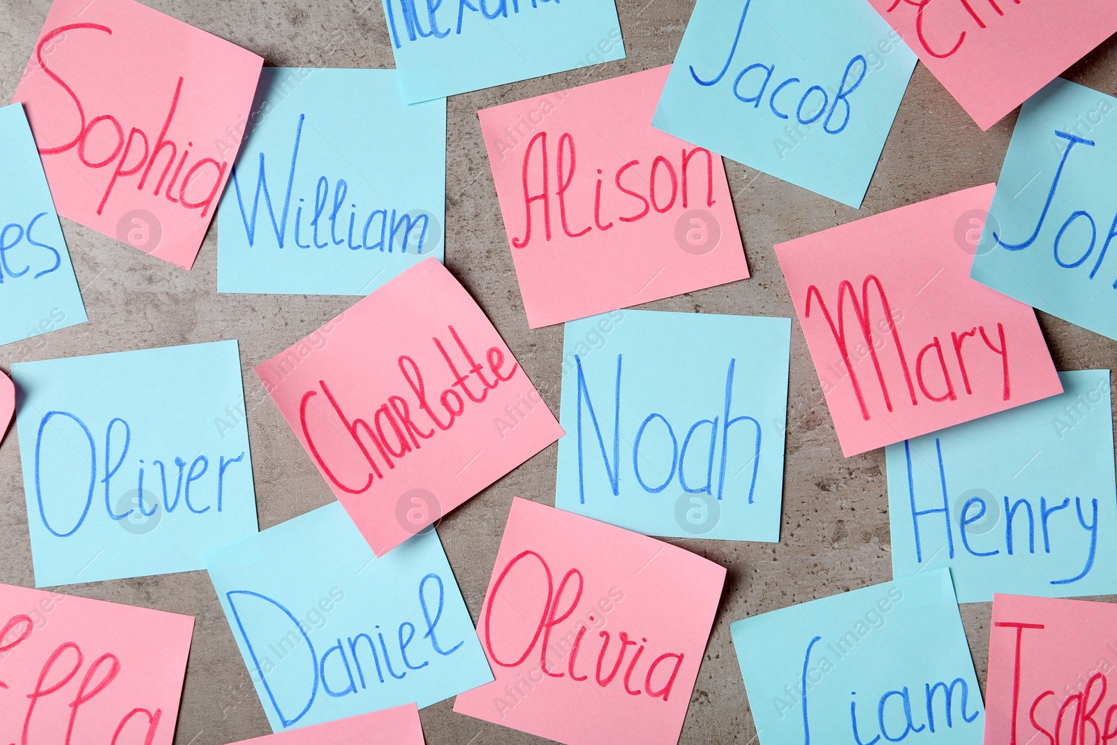 Photo of Colorful paper sheets with written different baby names on grey background, flat lay