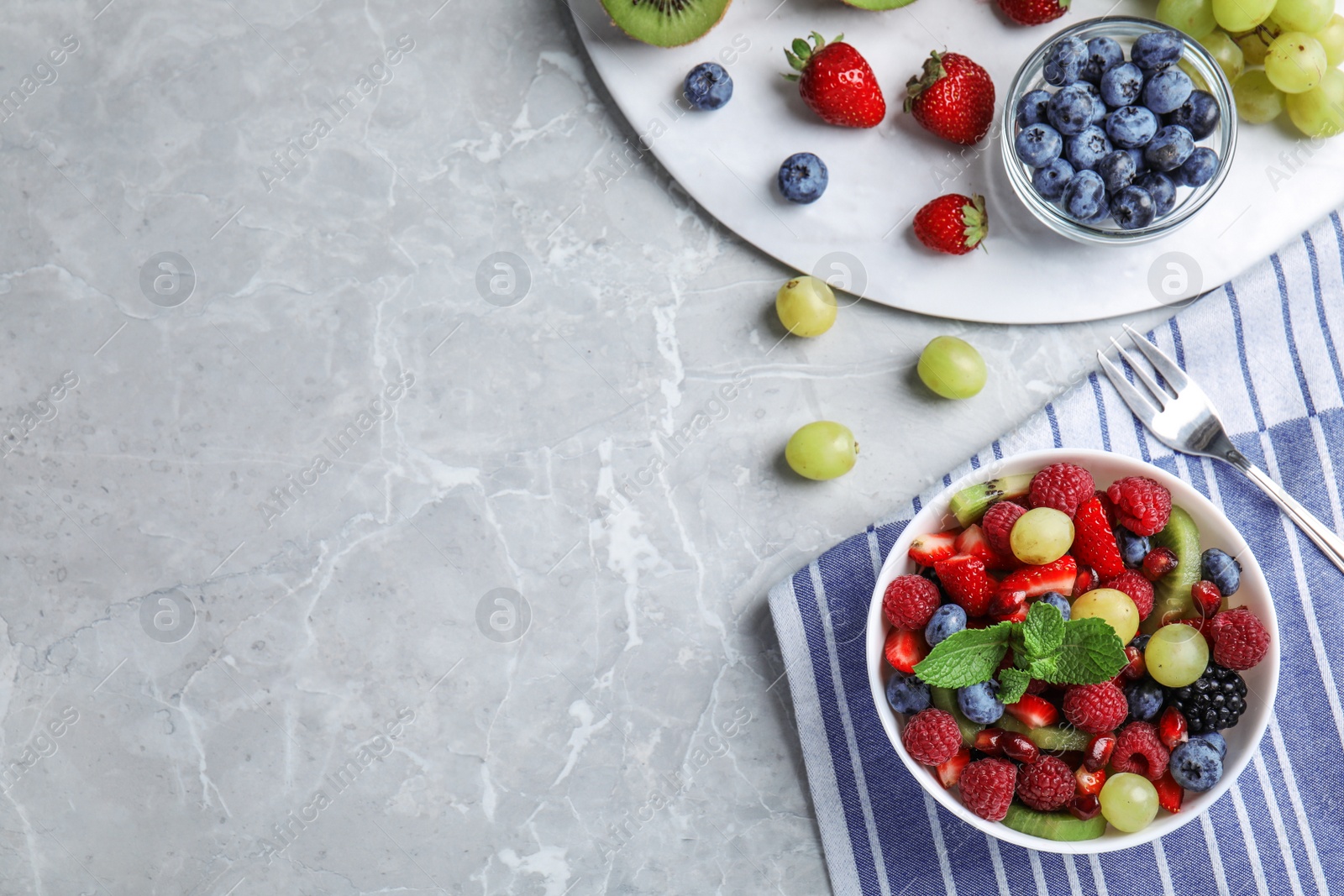 Photo of Fresh tasty fruit salad on grey marble table, flat lay. Space for text