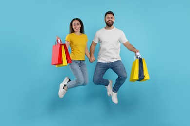 Photo of Happy couple with shopping bags jumping on light blue background