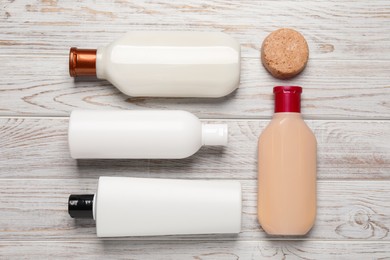 Shampoo bottles and solid shampoo bar on white wooden table, flat lay