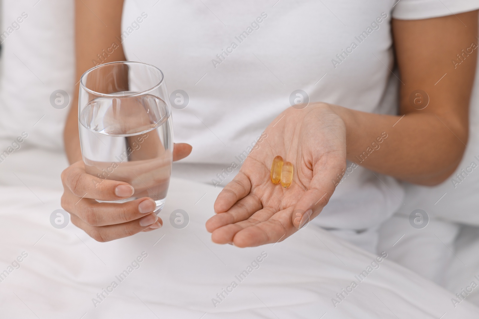 Photo of Woman with vitamin pills and glass of water in bed, closeup