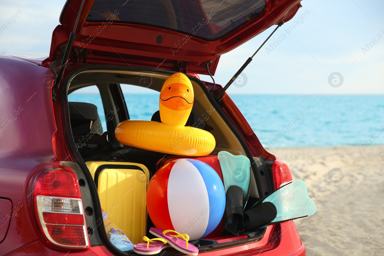 Photo of Red car with luggage on beach, closeup. Summer vacation trip