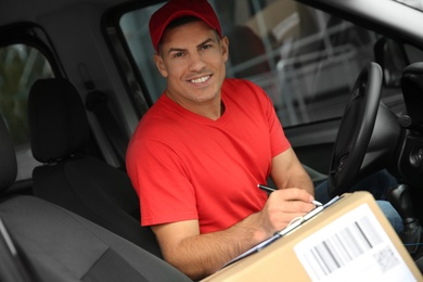 Photo of Courier with clipboard checking packages in car