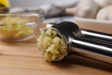 Photo of One metal press with crushed garlic on wooden table, closeup