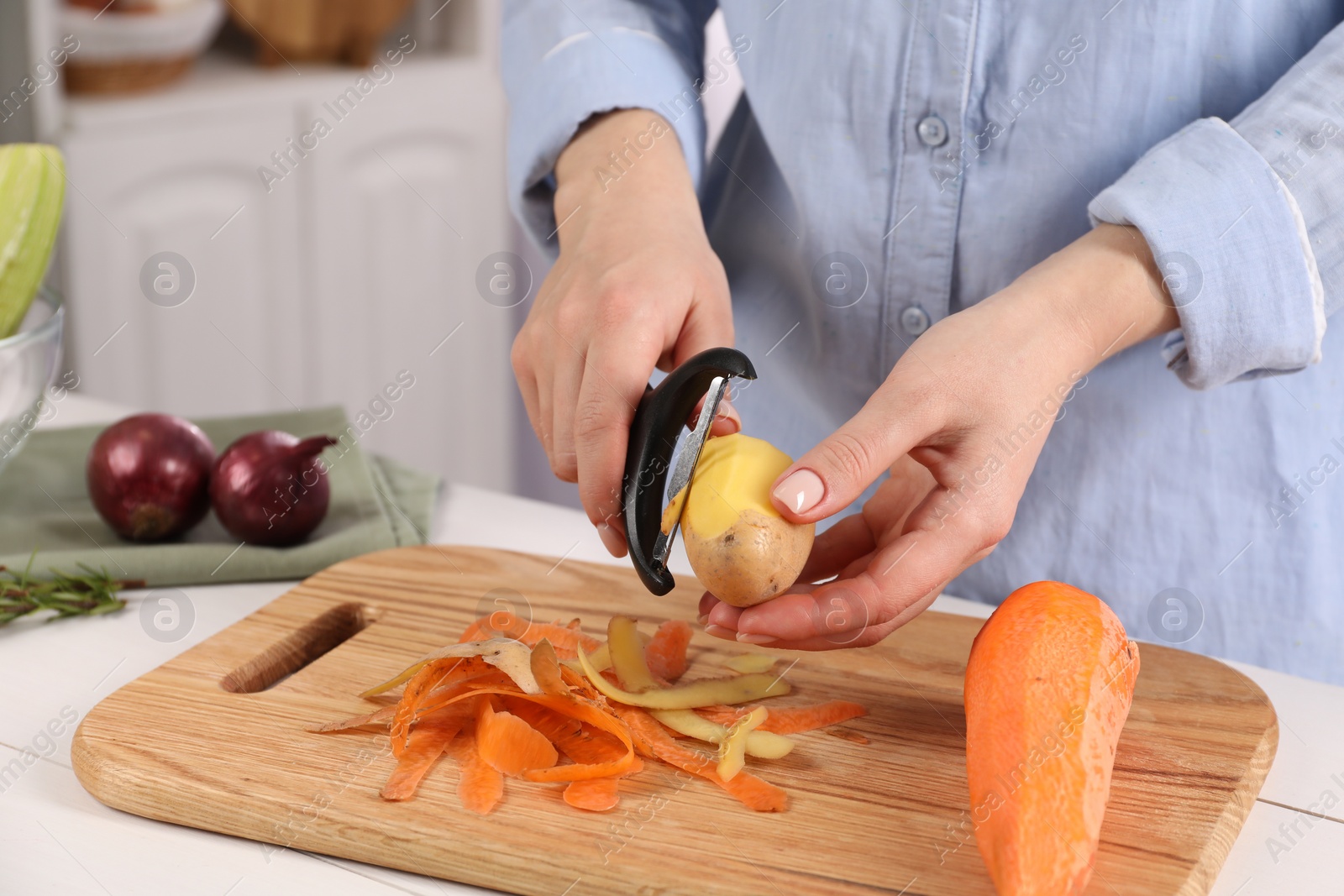 Photo of Woman peeling fresh potato at table indoors, closeup