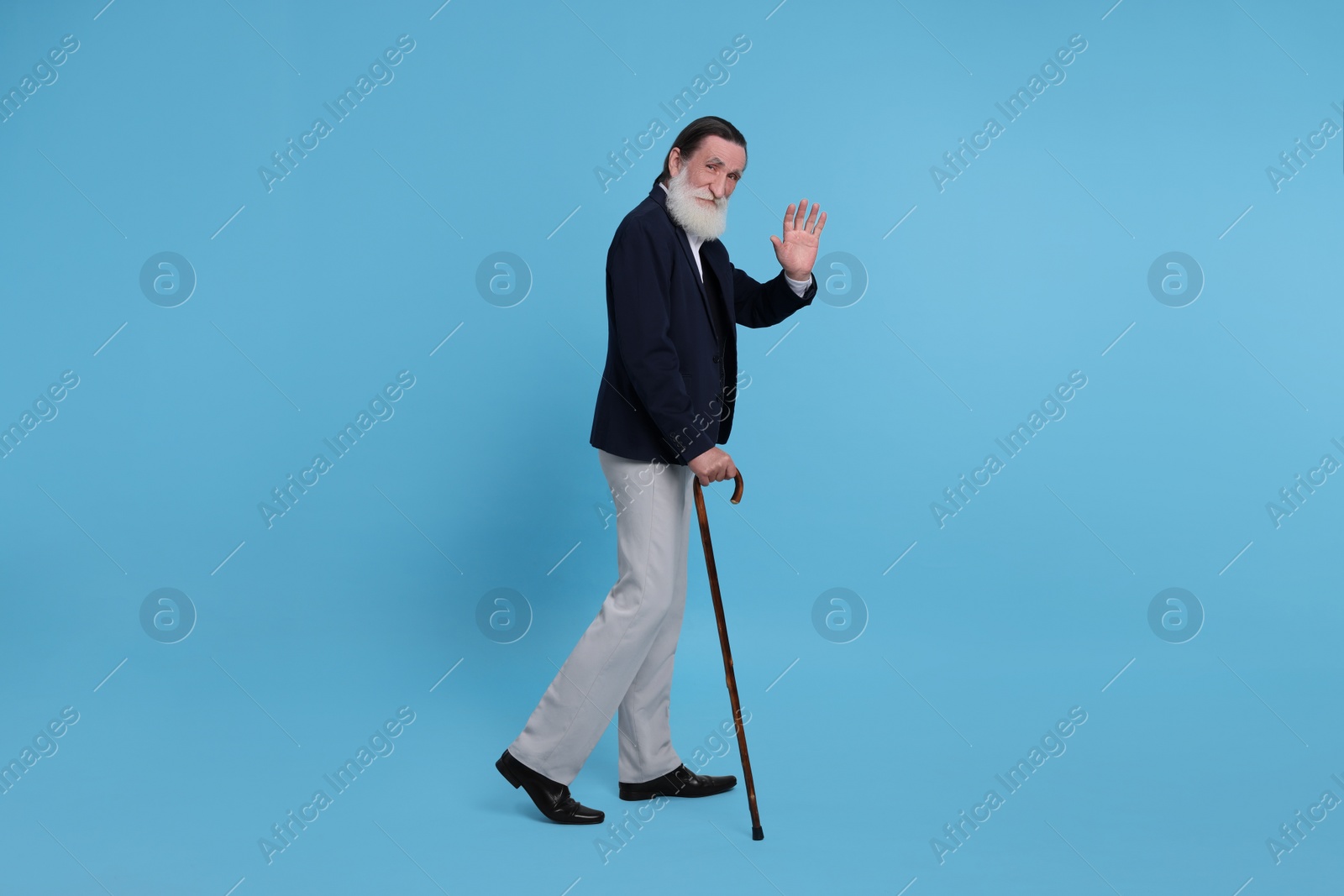 Photo of Senior man with walking cane waving on light blue background