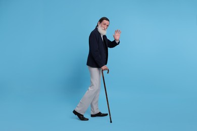 Photo of Senior man with walking cane waving on light blue background