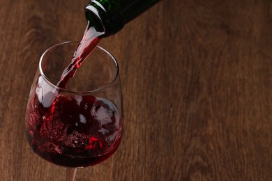 Pouring tasty red wine in glass at wooden table, closeup. Space for text