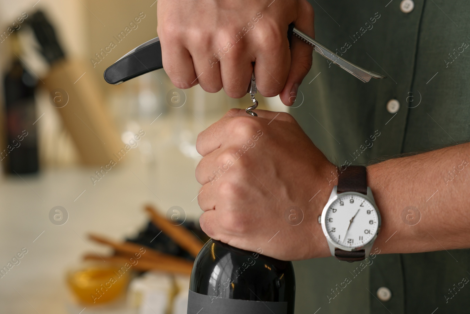 Photo of Man opening wine bottle with corkscrew indoors, closeup