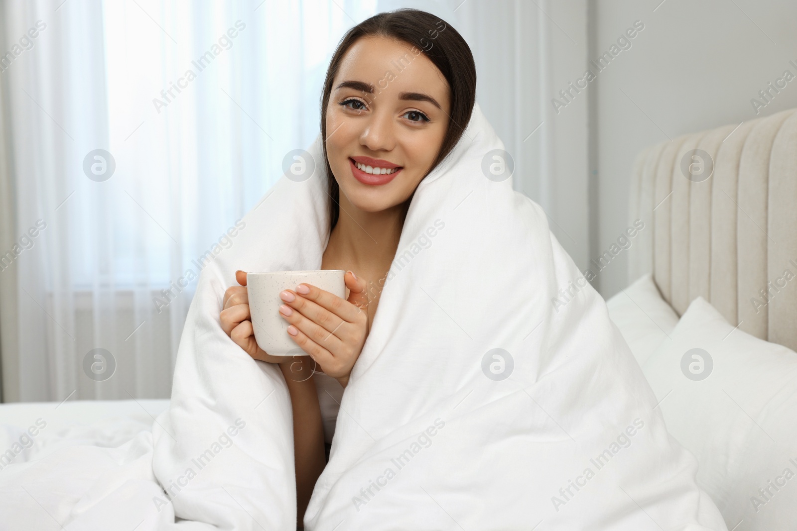 Photo of Beautiful young woman with cup of drink wrapped in blanket at home