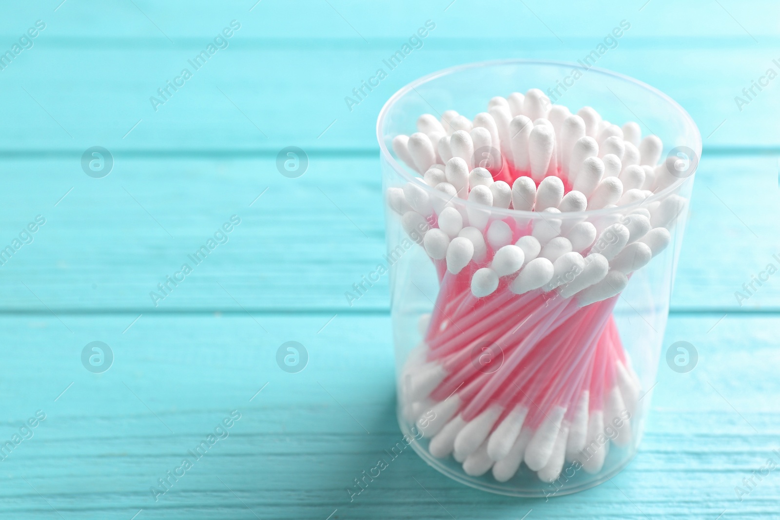 Photo of Plastic container with cotton swabs on wooden background. Space for text