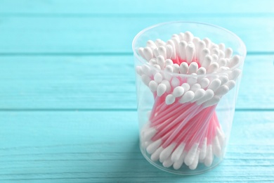 Photo of Plastic container with cotton swabs on wooden background. Space for text