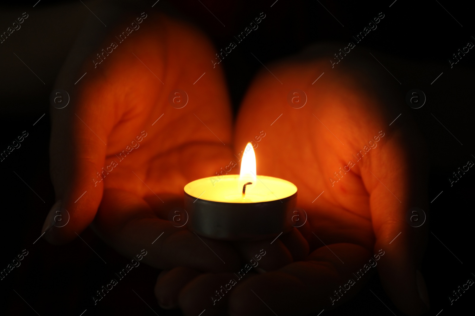 Photo of Woman holding burning candle in darkness, closeup