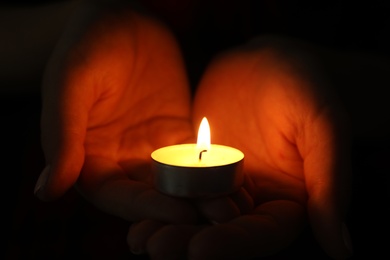 Photo of Woman holding burning candle in darkness, closeup