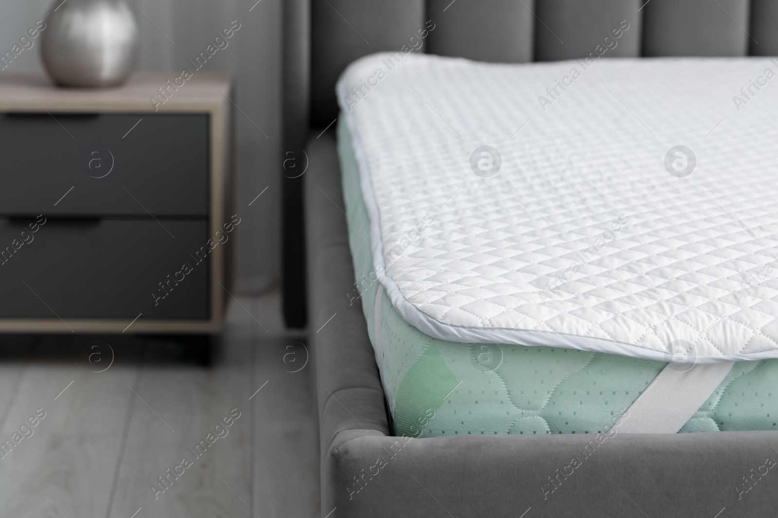 Photo of New soft mattress with protector on grey bed in bedroom, closeup. Space for text