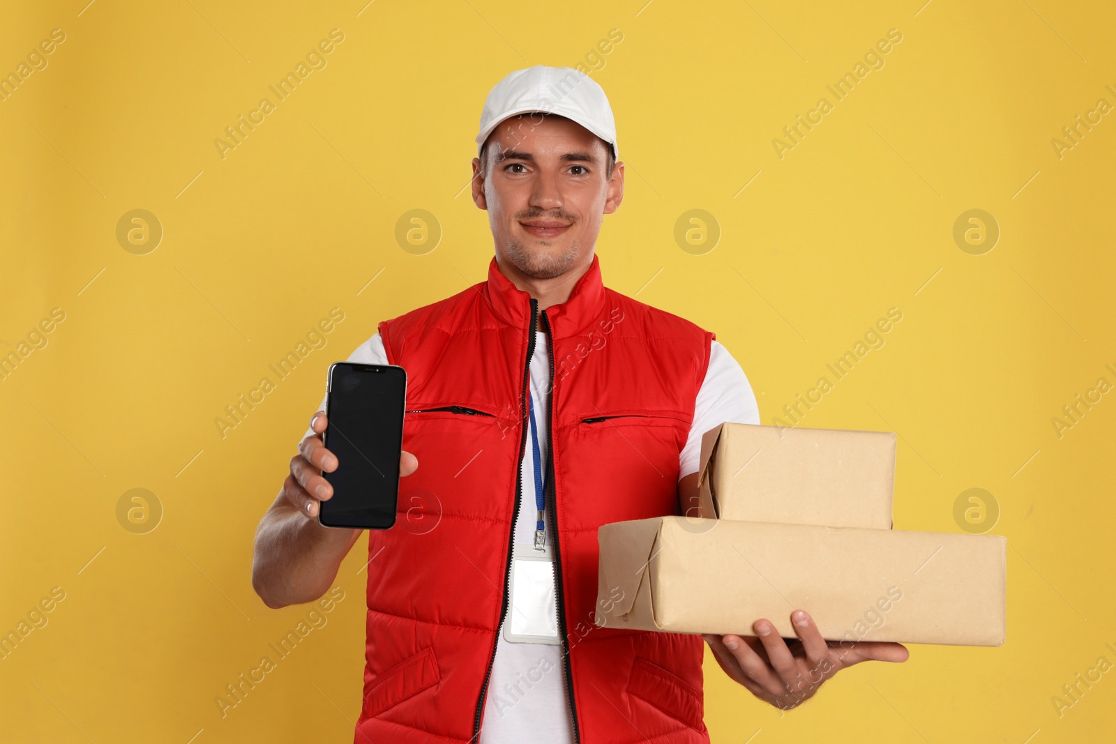 Photo of Happy young courier with mobile phone and parcels on yellow background