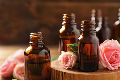 Photo of Bottles of rose essential oil and fresh flowers on table, closeup