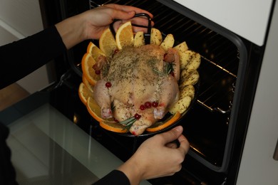 Photo of Woman putting chicken with orange and potato slices into oven, closeup