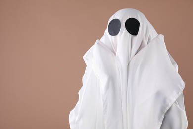 Photo of Creepy ghost. Person covered with white sheet on dark beige background, space for text