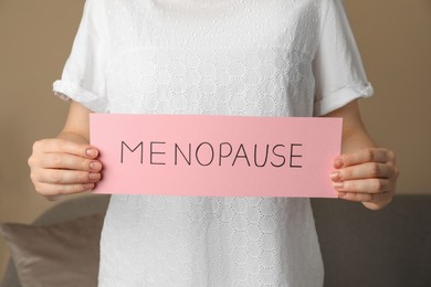 Photo of Woman holding paper sheet with word MENOPAUSE indoors, closeup